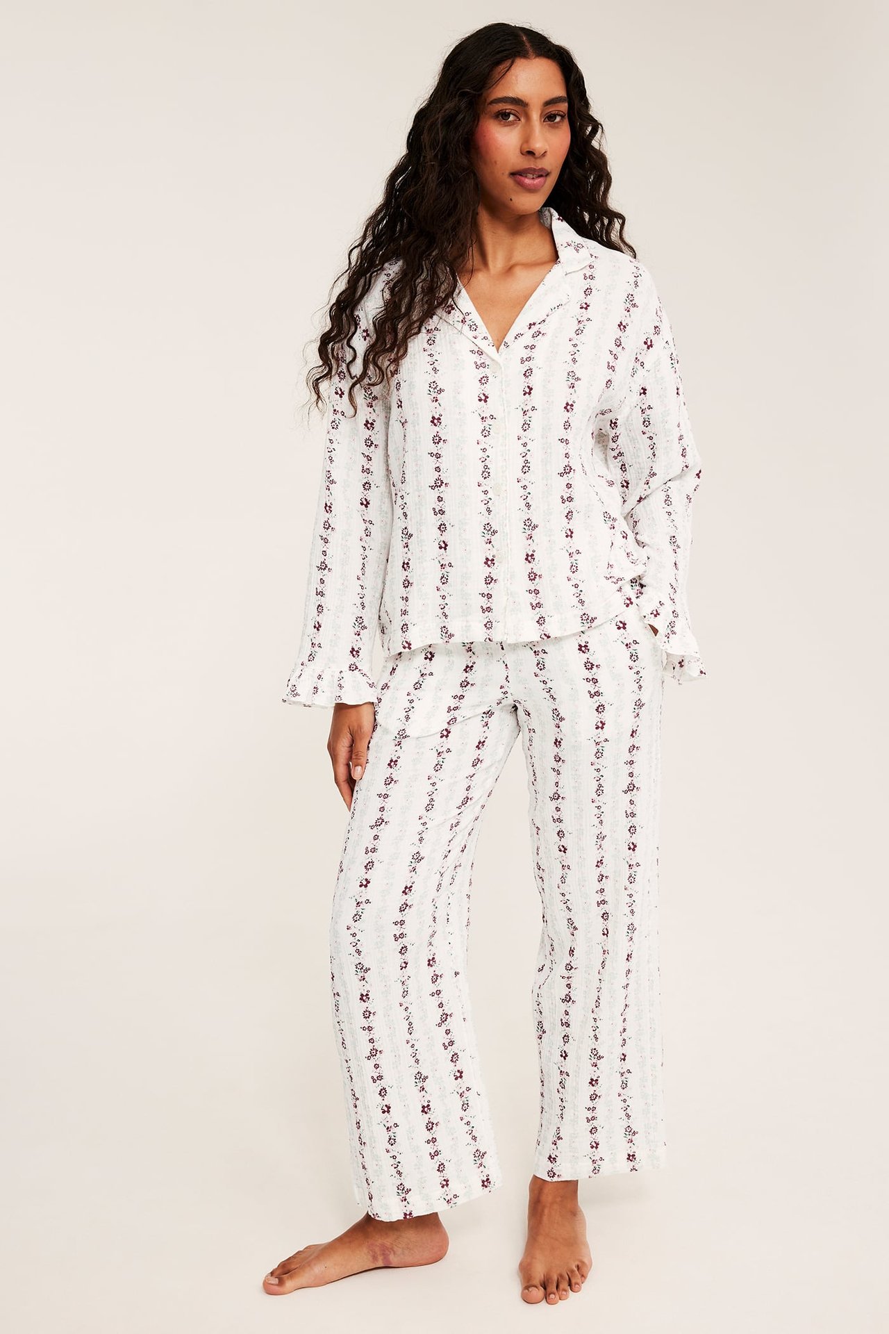 Edestä näkymä naisesta valkoisessa pyjamassa punaisella kukkaraidoituskuviolla.