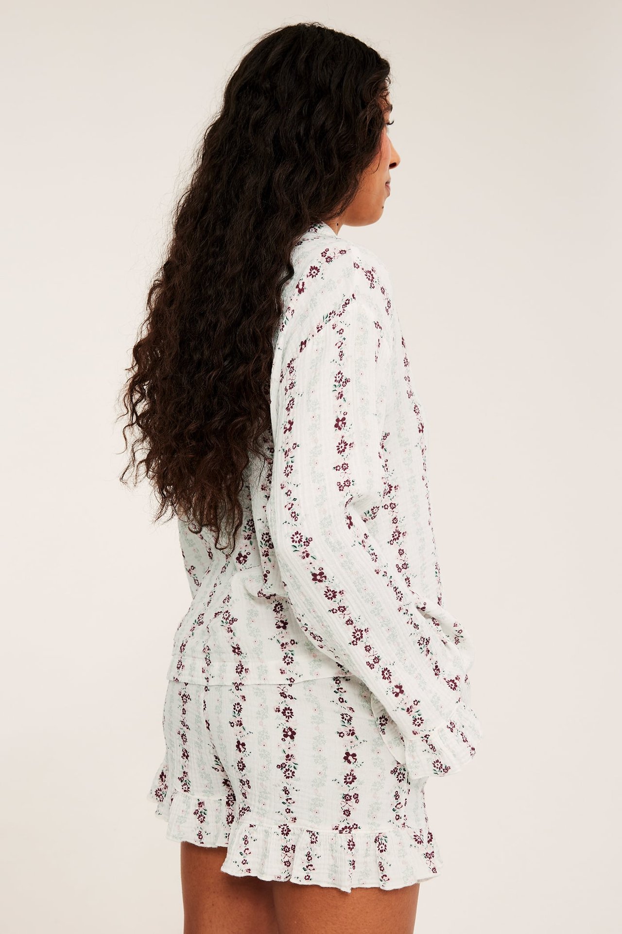 Sidovy av kvinna i ljus randig blommig långärmad pyjamastopp och volangshorts.