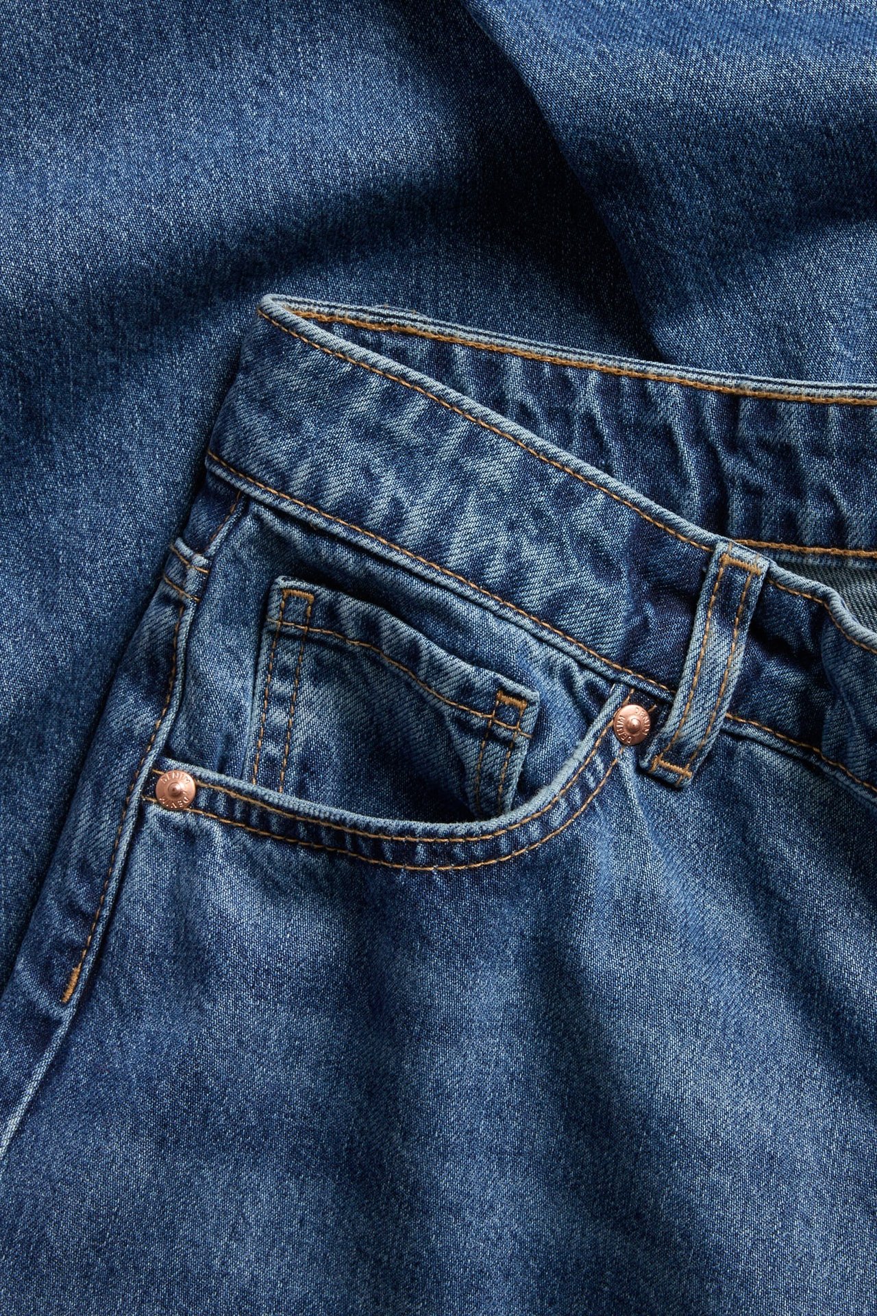 Zbliżenie przodu granatowych jeansów high-waist z szerokimi nogawkami, pięcioma kieszeniami i miedzianymi nitami.