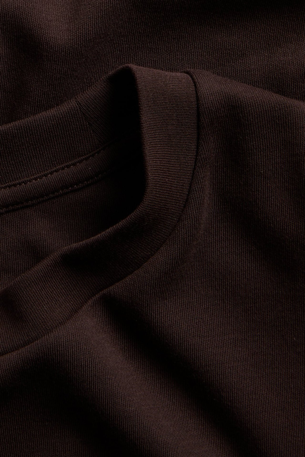Närbild av en mörkbrun oversized t-shirt i interlockbomull med ribbad rundhals.