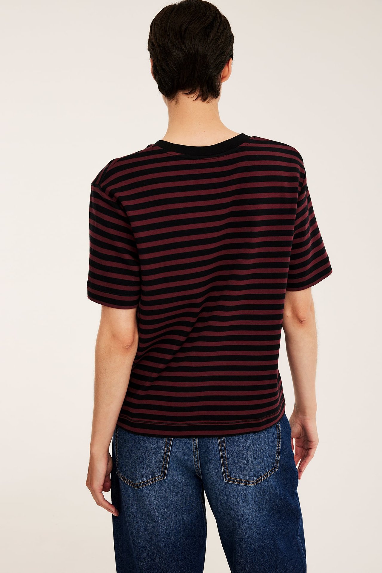 Ryggbild på en kvinna i svart och vinrödrandig t-shirt och mörkblå jeans.
