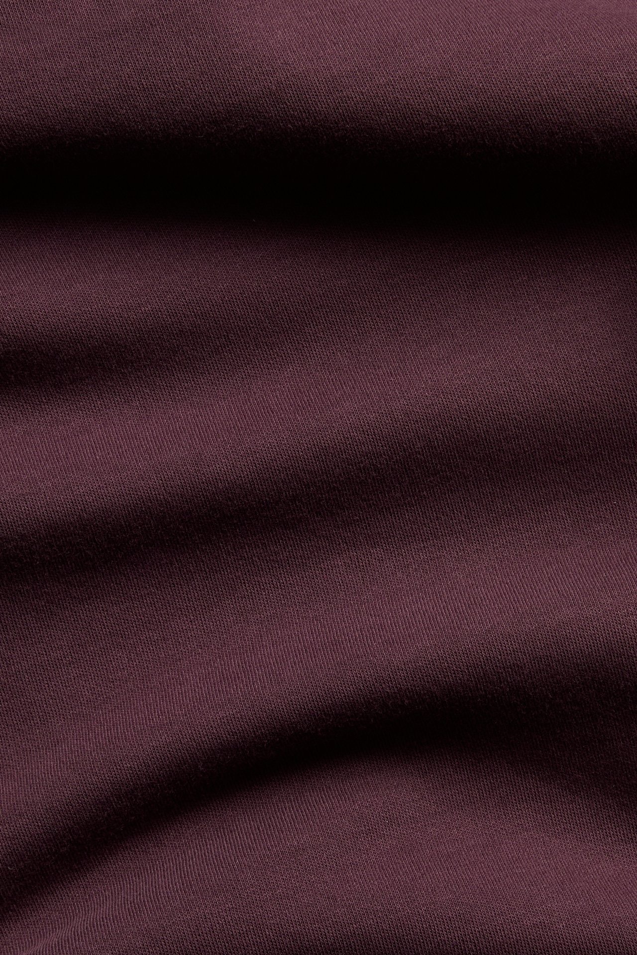 Närbild på ett vinrött, enfärgat tyg i 100% bomull, som visar mjuka veck och textur.