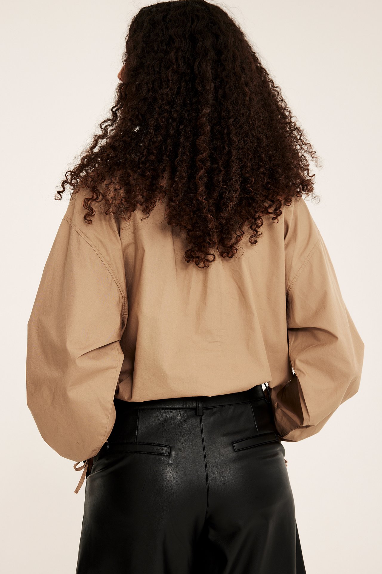 Bakifrån: kvinna i beige avslappnad blus och svarta läderbyxor.