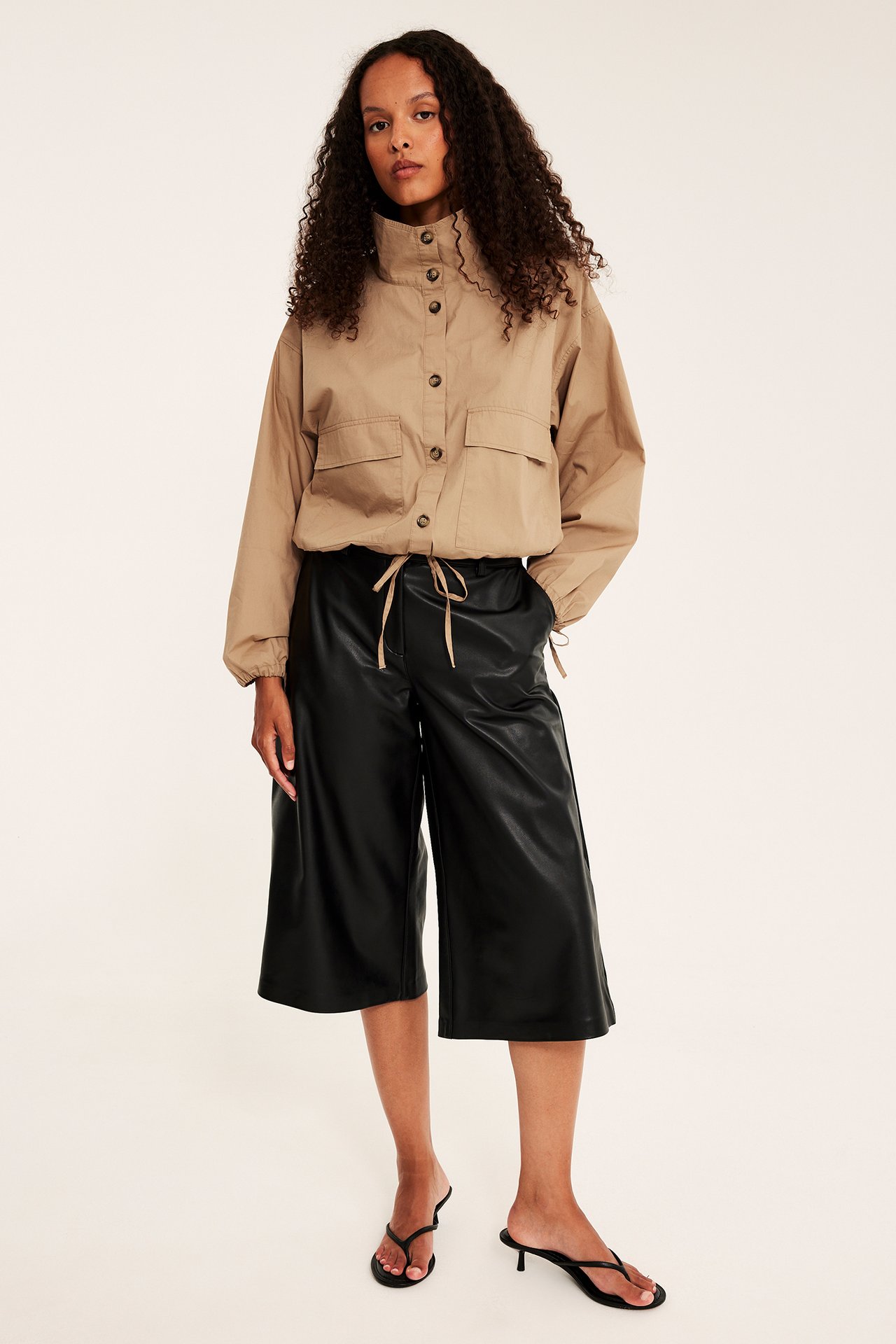Framifrån: Kvinna i beige utility-skjorta, svarta culottes i fuskläder och svarta sandaler med klack.