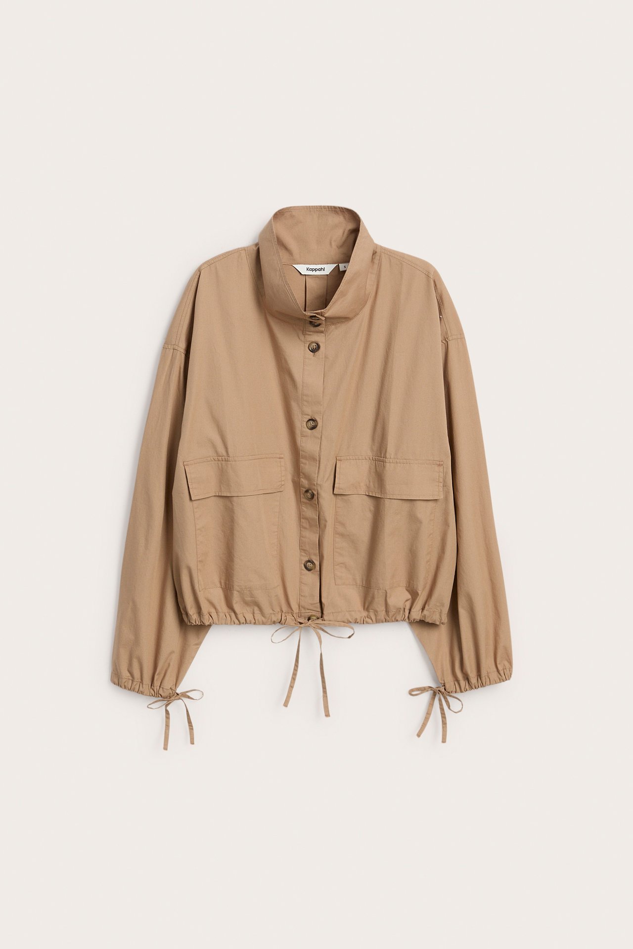 Framifrån: Beige knäppt damjacka med hög krage, fickor och dragsko detaljer.
