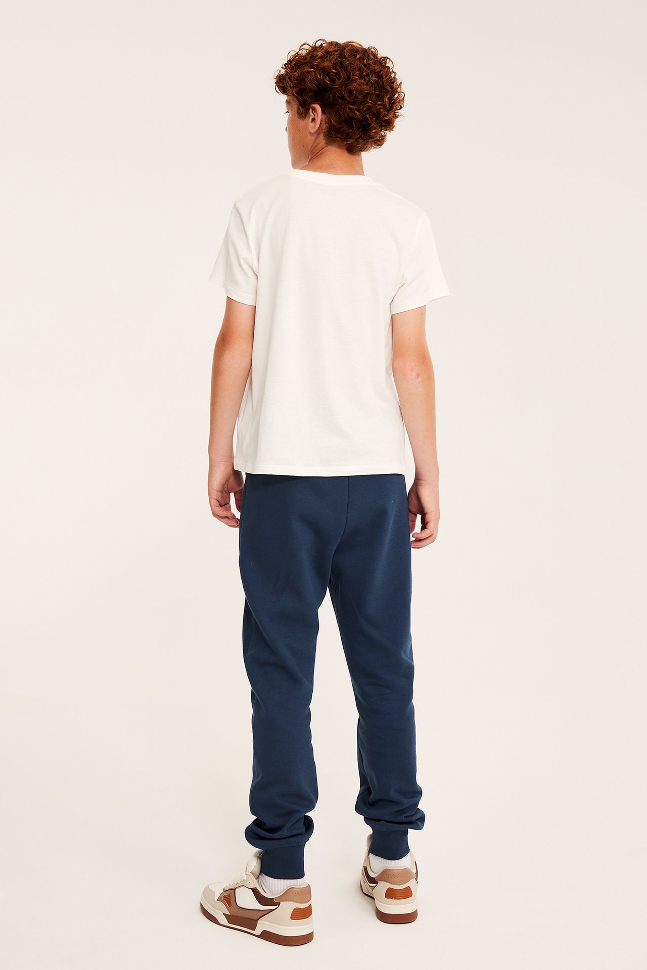 Bakifrån av ett barn i vit kortärmad t-shirt, mörkblå mjukisbyxor och sneakers.