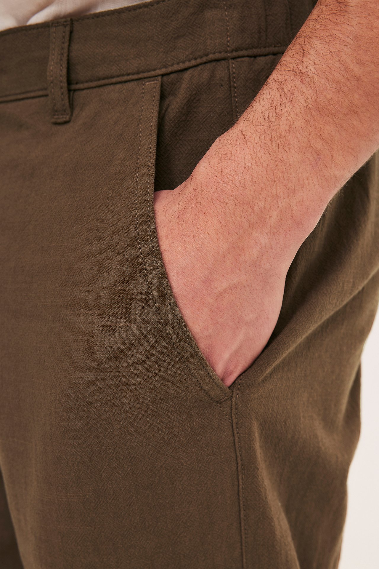 Zbliżenie z boku na mężczyznę w brązowych bawełnianych spodniach z ręką w kieszeni.