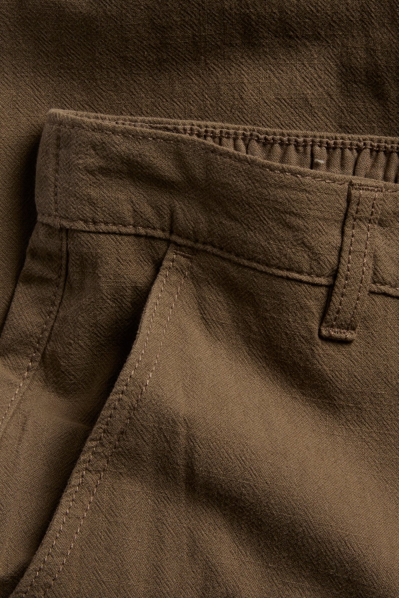 Zbliżenie brązowych męskich bawełnianych spodni regular fit z teksturą lnu i boczną kieszenią.