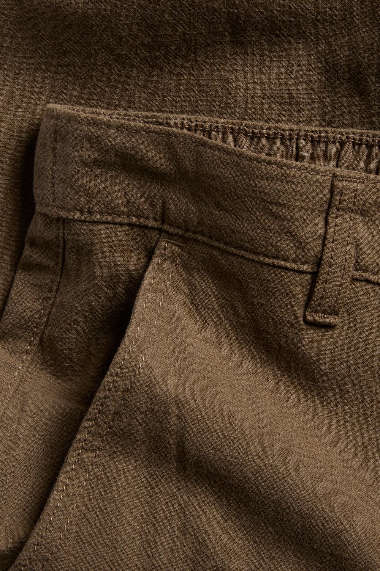 Zbliżenie brązowych męskich bawełnianych spodni regular fit z teksturą lnu i boczną kieszenią.