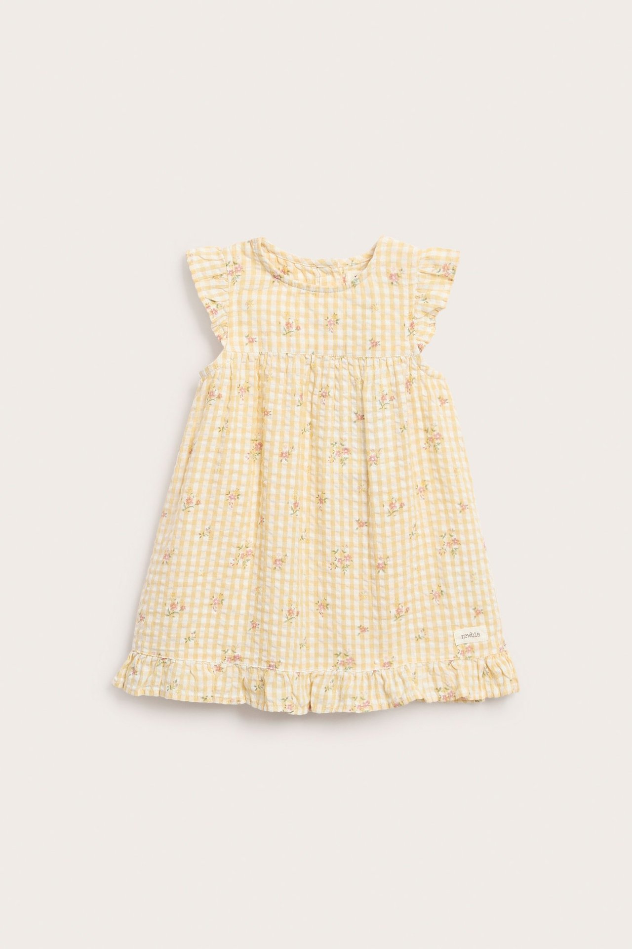 Edestäpäin keltainen ruudullinen lasten mekko, jossa pieni kukkakuvio, röyhelöolkapäät ja röyhelöreuna.