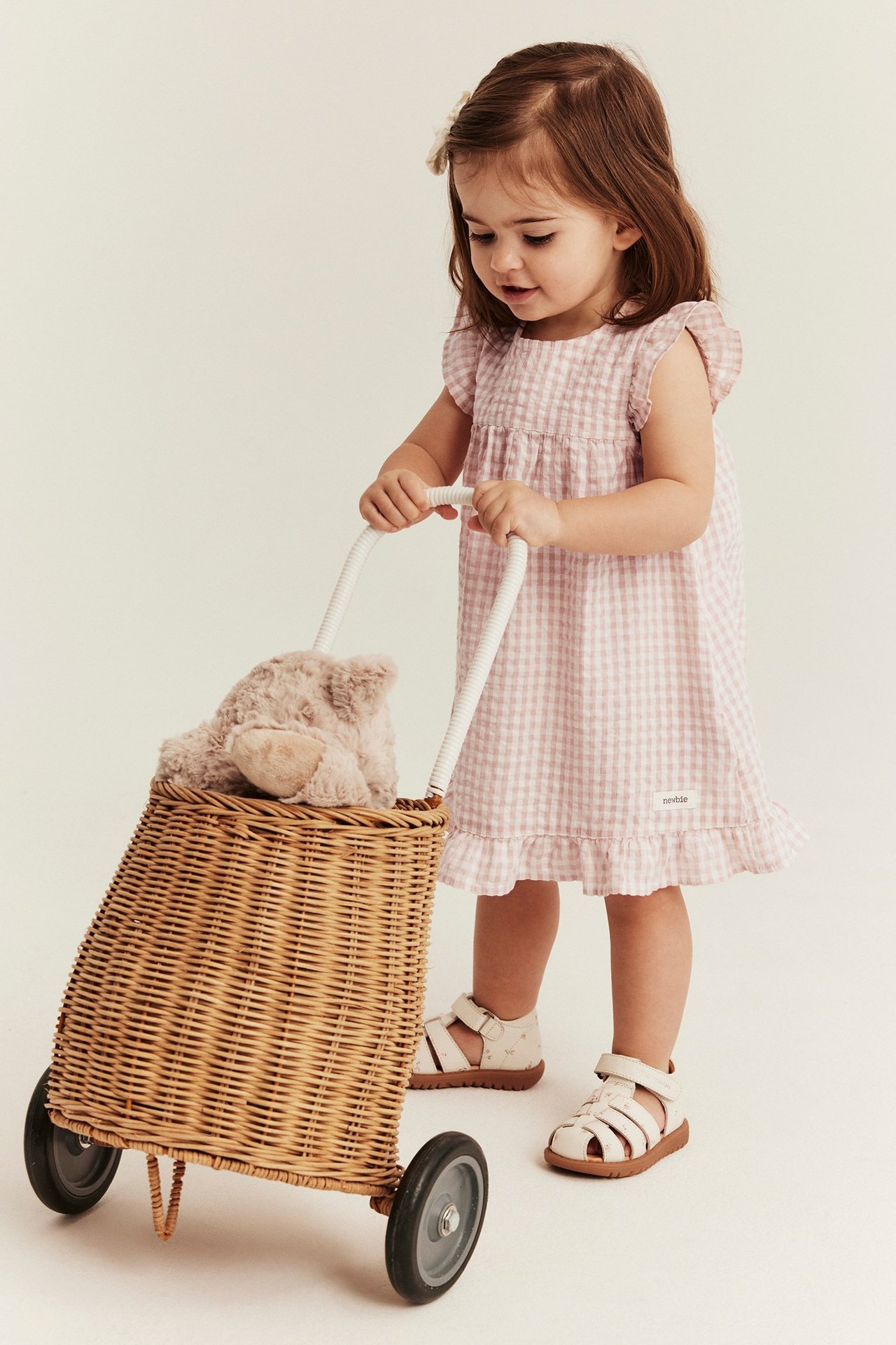 Frontbilde: Et barn i lys rosa rutet bomullskjole med volanger og hvite sandaler.
