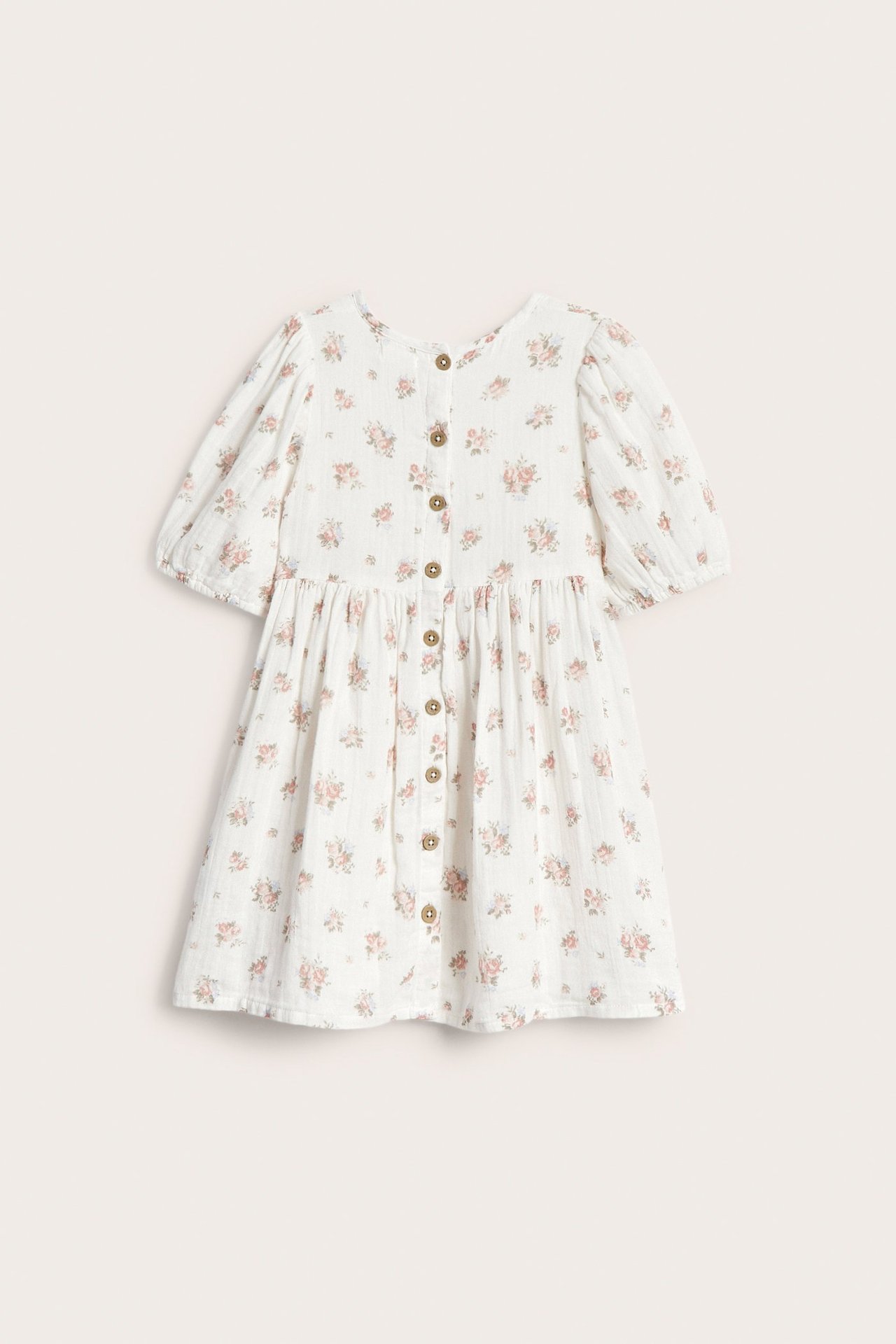 Frontbilde av en offwhite barnekjole med rosa blomstermønster, korte puffermer og knappelukking foran.