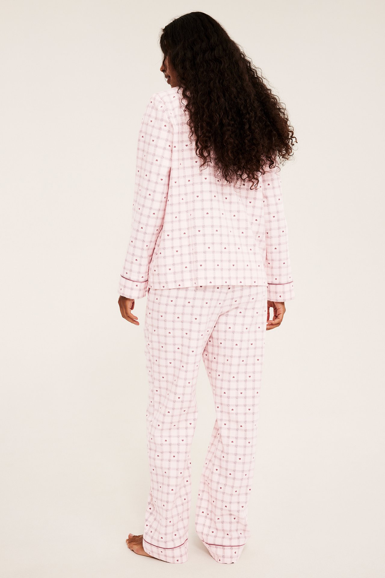 Nainen selin, yllään vaaleanpunainen ruudullinen pyjamas pienillä punaisilla sydämillä.