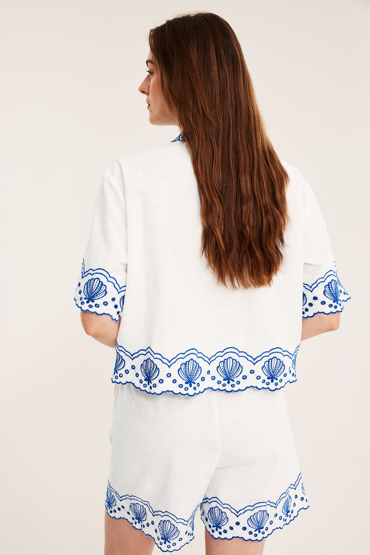 Widok z tyłu: Kobieta w bawełnianych szortach i pasującym topie w kolorze ecru z niebieskim haftem w muszelki.