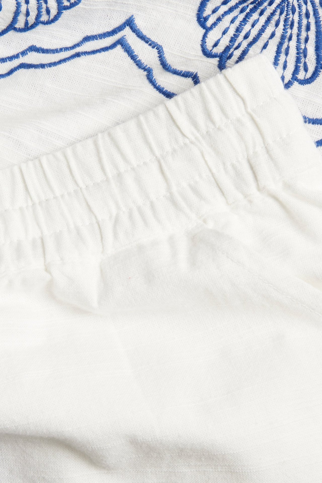 Zbliżenie na szorty bawełniane w kolorze złamanej bieli z elastyczną talią i niebieskim haftowanym wzorem.