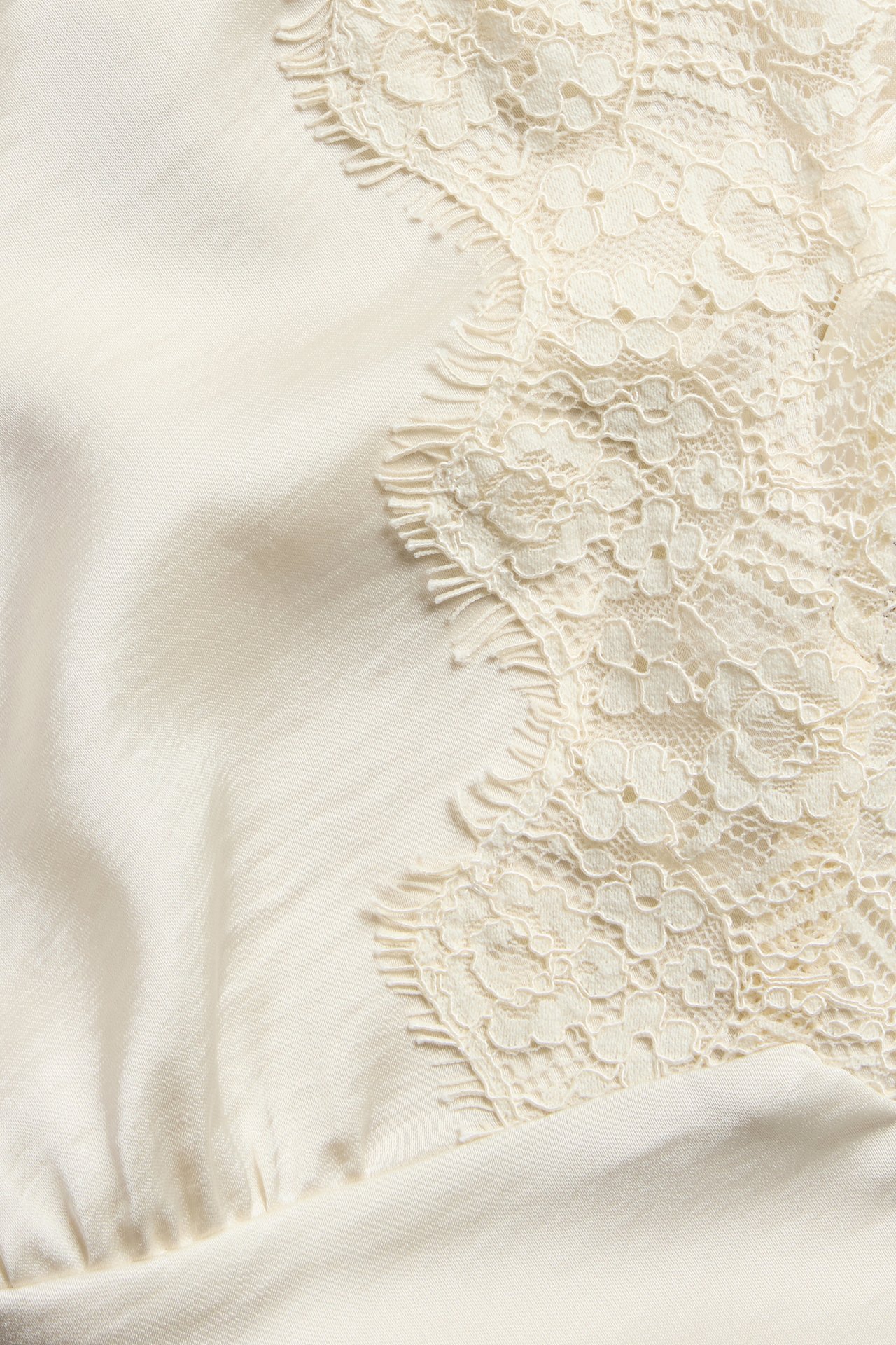 Zbliżenie na ecru satynową koszulkę z delikatnym koronkowym obszyciem w kwiaty.
