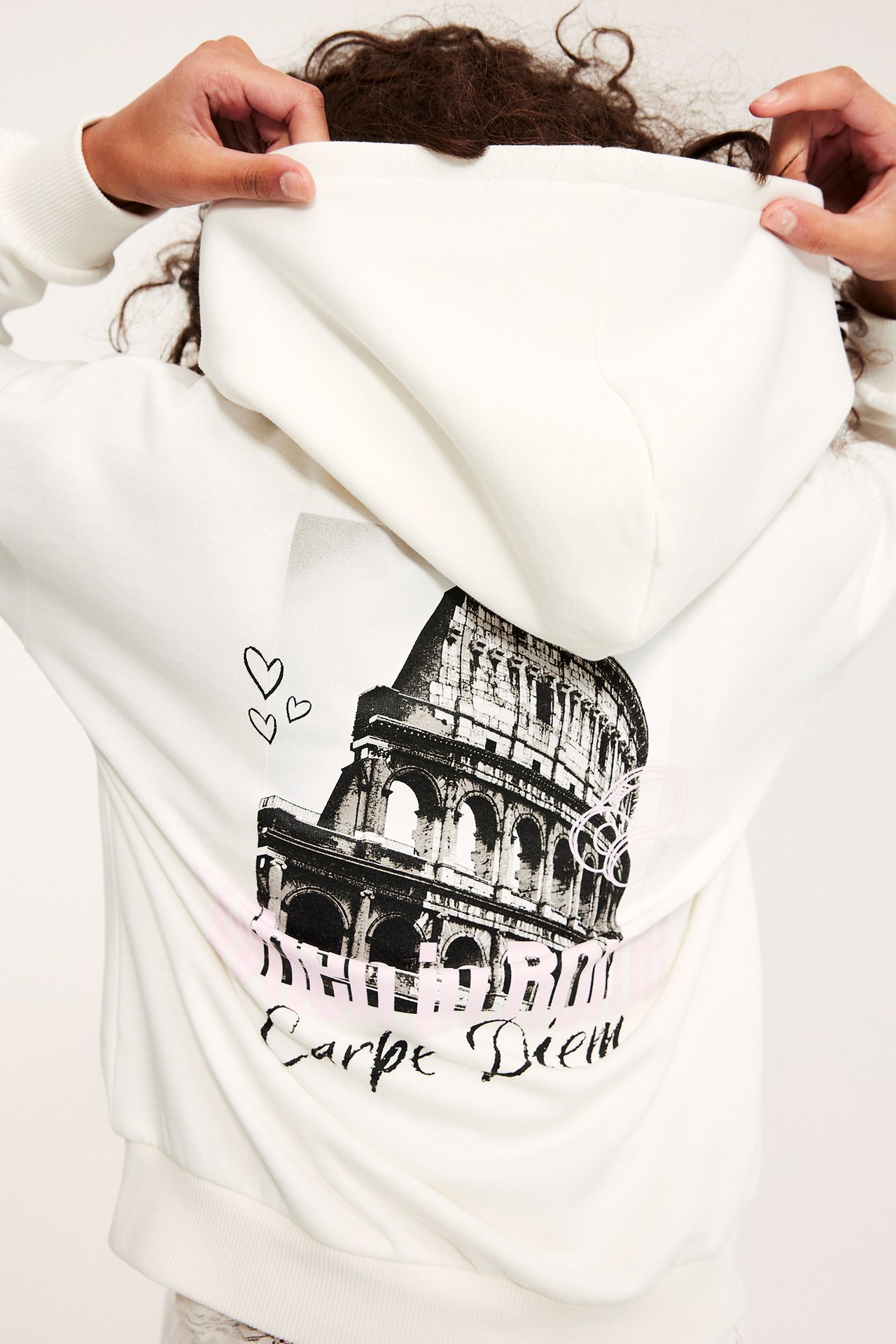 Widok z tyłu dziecka naciągającego ecru bluzę z kapturem z czarno-białym Koloseum i tekstem.