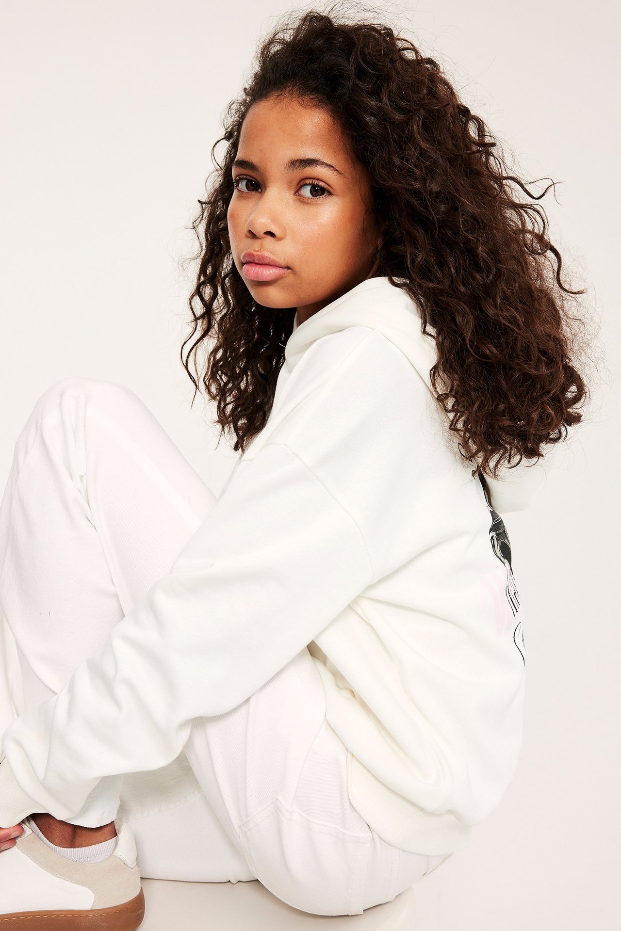 Sivukuva: Lapsi yllään luonnonvalkoinen huppari takapainatuksella, valkoiset housut ja valkoiset tennarit.