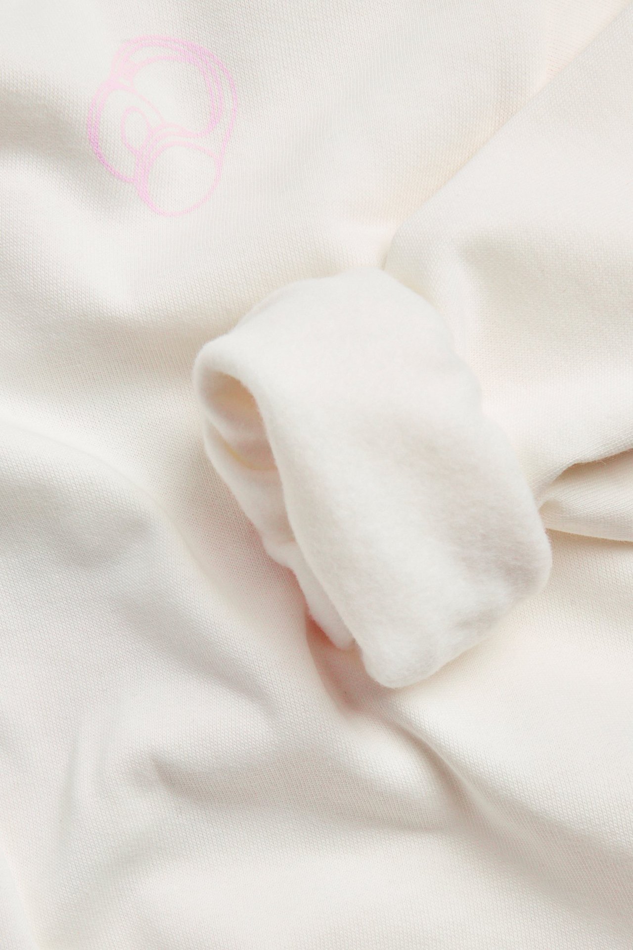 Zbliżenie beżowej bluzy bawełnianej z małym różowym abstrakcyjnym nadrukiem i podwiniętym mankietem rękawa.