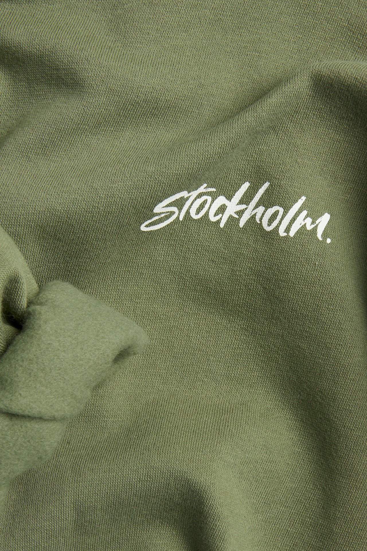 Närbild framifrån på en mörkgrön bomullsblandad hoodie med vitt 'Stockholm'-tryck.