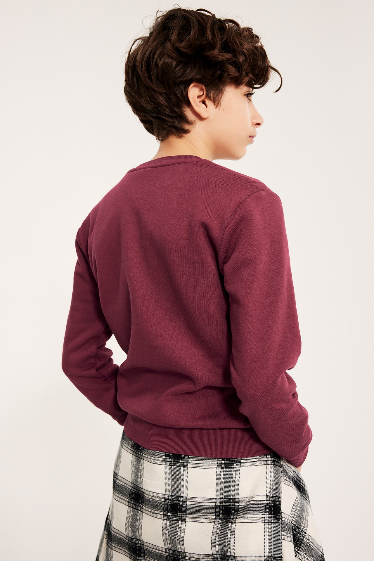 Side-/bakfra-visning av barn i vinrød sweatshirt over et hvit- og svartrutet skjørt.