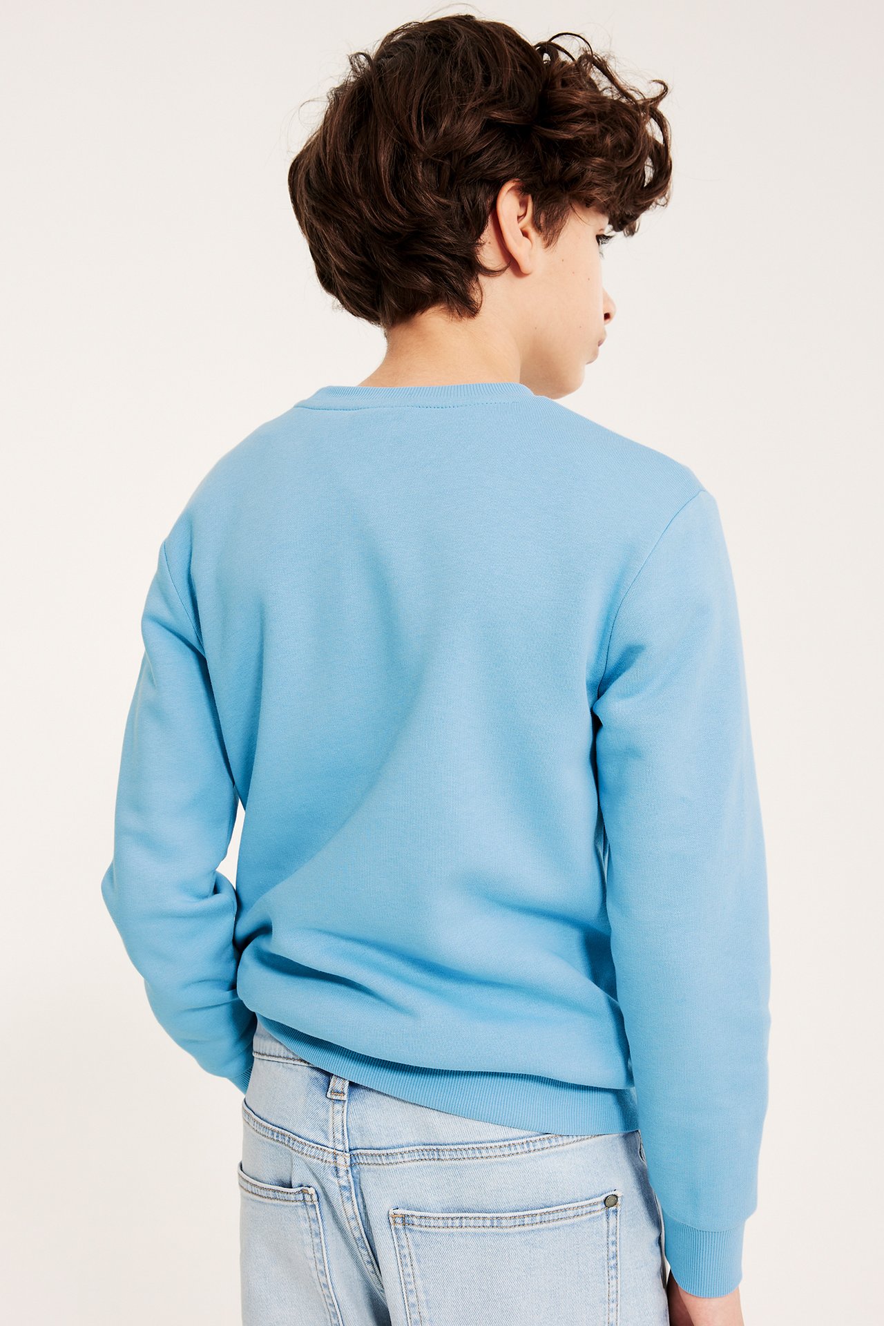 Bakfra av et barn i en lyseblå bomullsblanding sweatshirt og lyse jeans.