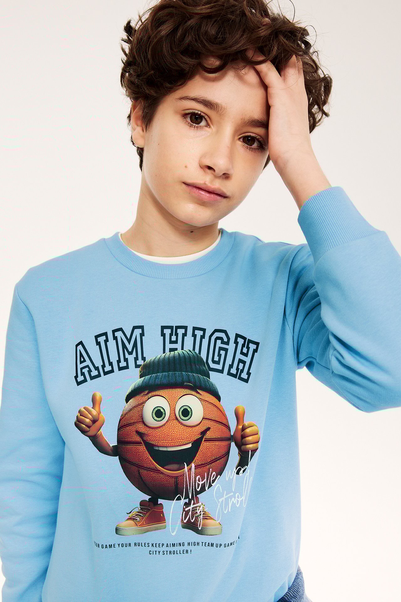 Widok z przodu: dziecko w jasnoniebieskiej bluzie z dużym nadrukiem koszykówki.