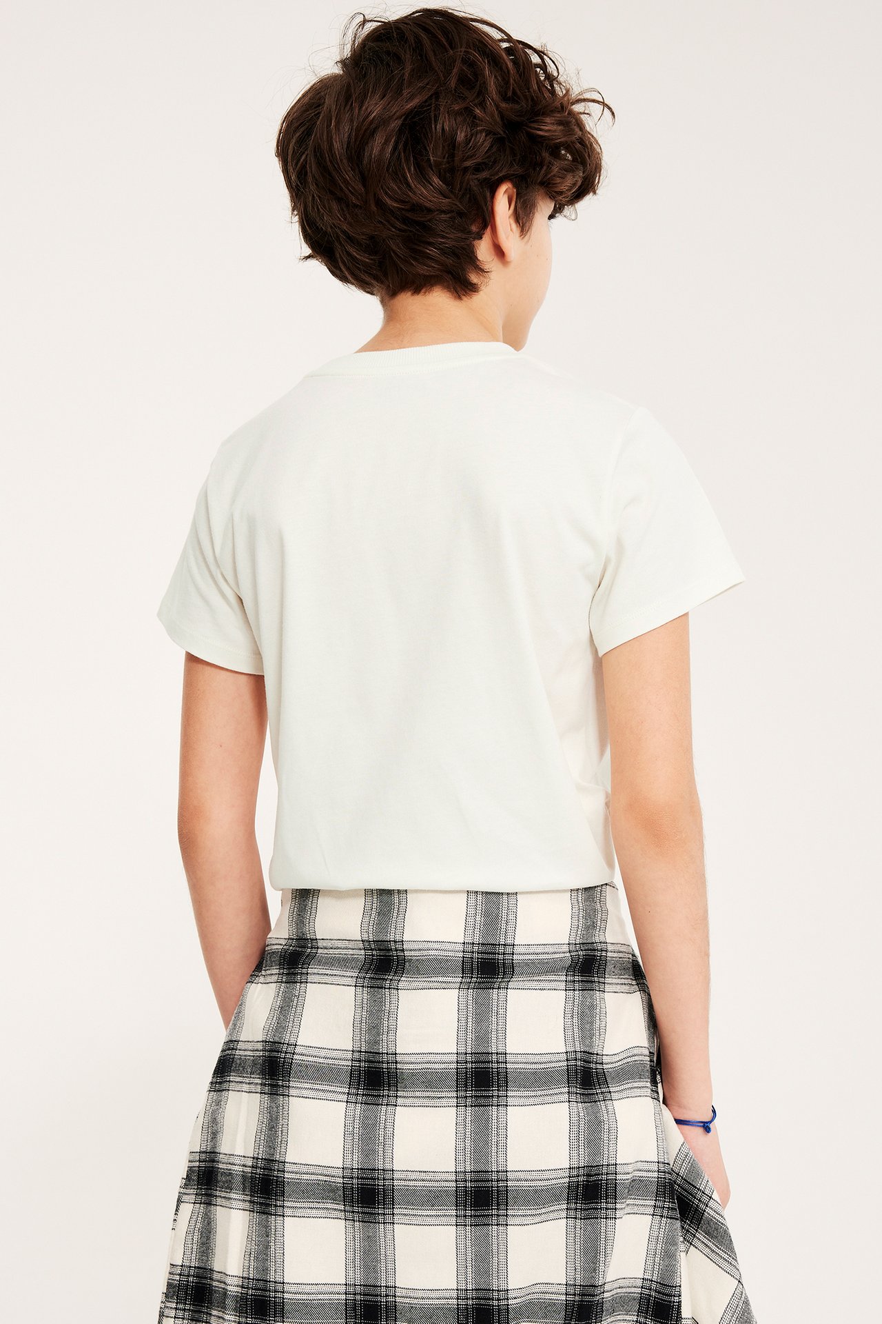 Et barn i en offwhite T-skjorte og et svart-hvitt rutete skjørt, bakfra.