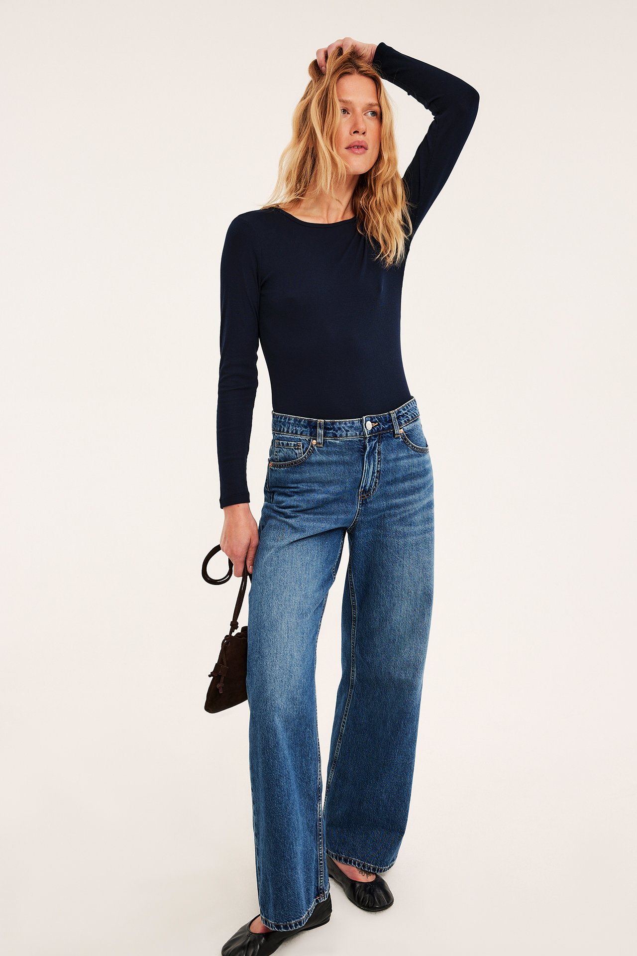 Framifrån blå vida jeans, mörkblå långärmad topp, mörkbrun handväska och svarta ballerinaskor.