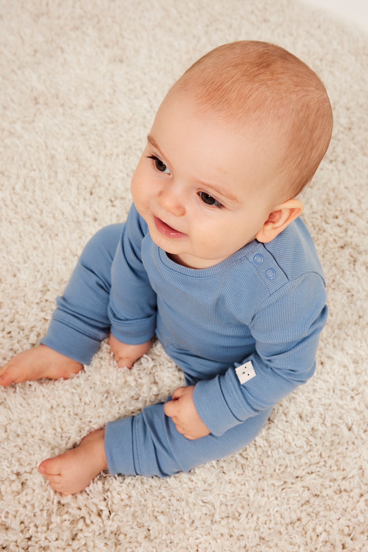 Baby i lyseblå ribbet langermet body med skulderknapper og matchende bukser.