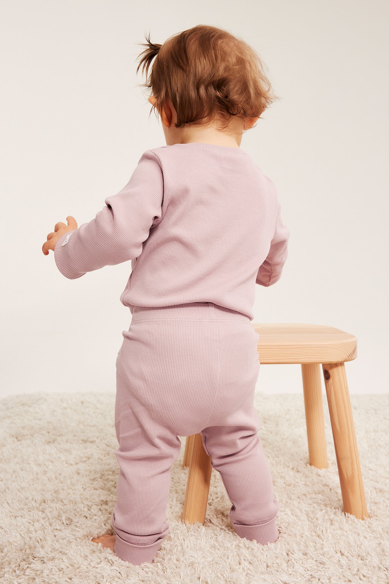 Bakfra av baby i lys lilla ribbet langermet topp og matchende bukser.