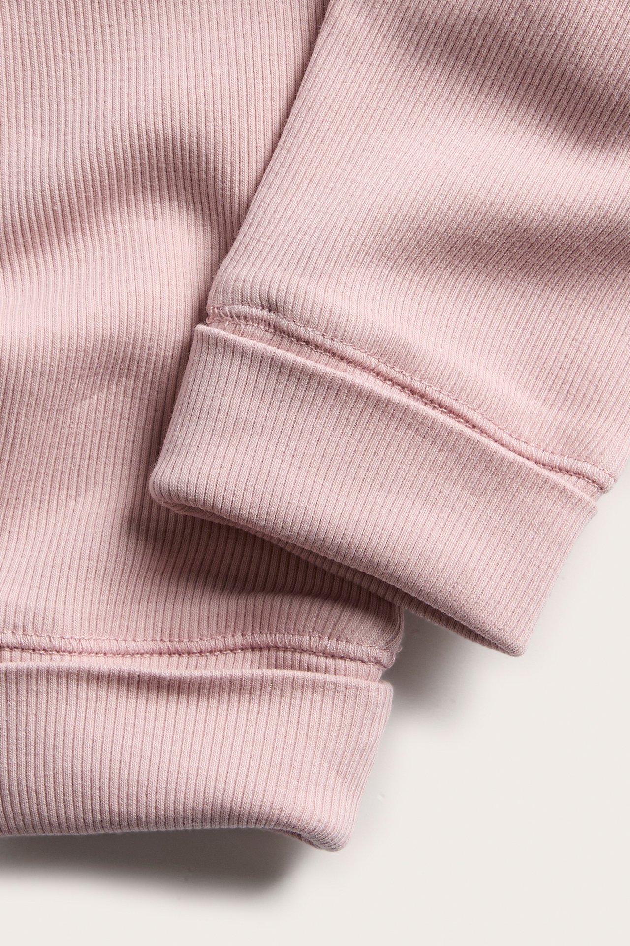 Nærbilde av en rosa ribbet strikket plaggerm og mansjett.
