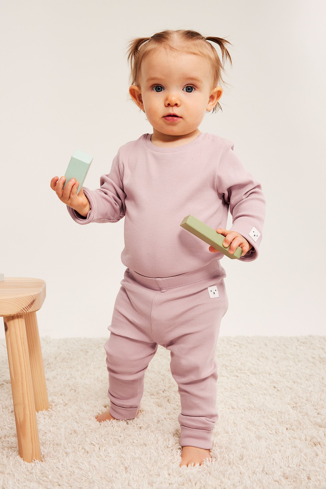 Frontalvisning av baby i lilla ribbet kosesett som holder to treklosser.