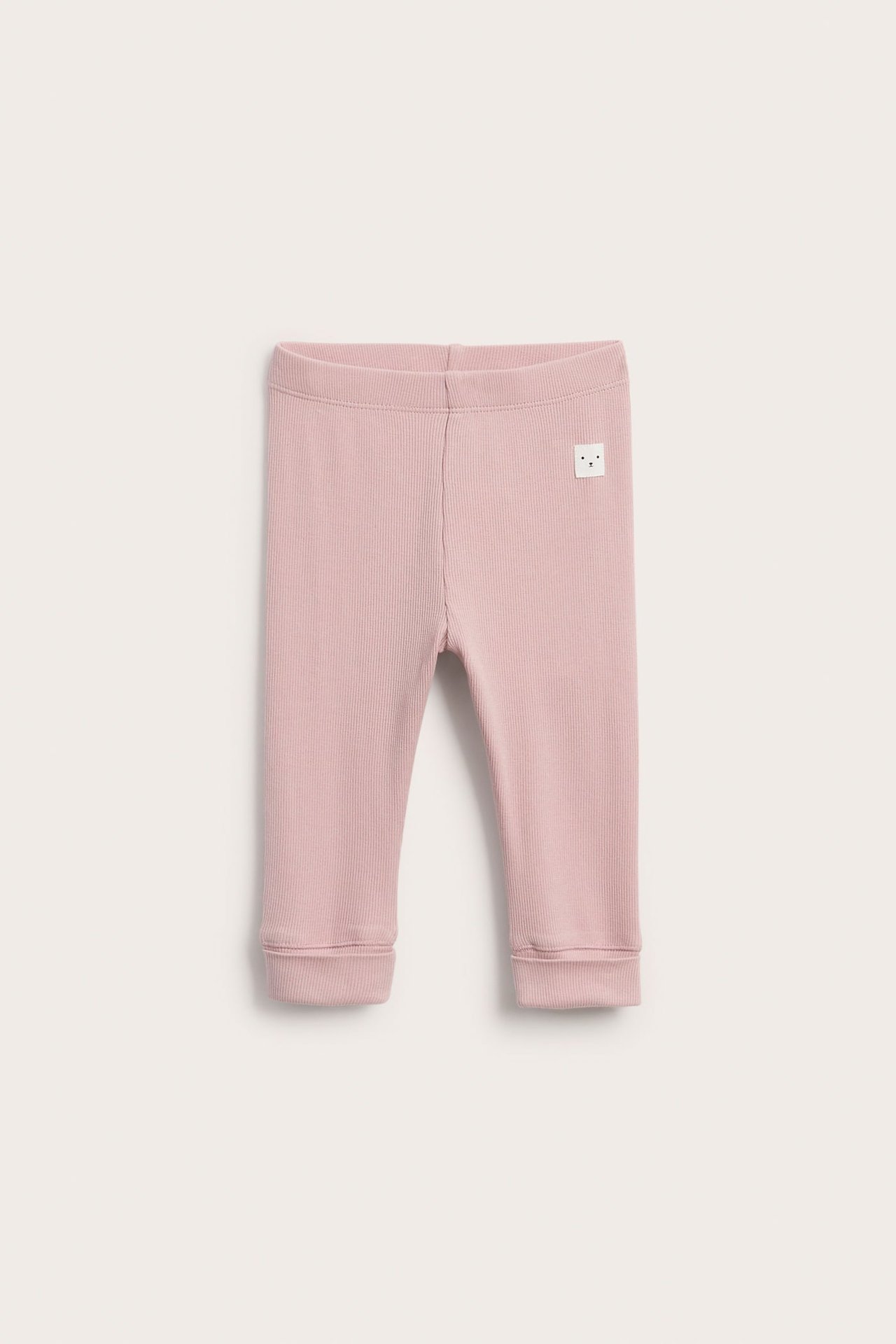 Edestä päin, ribattu vanhanroosa vauvanleggings pienellä valkoisella kasvoetiketillä.