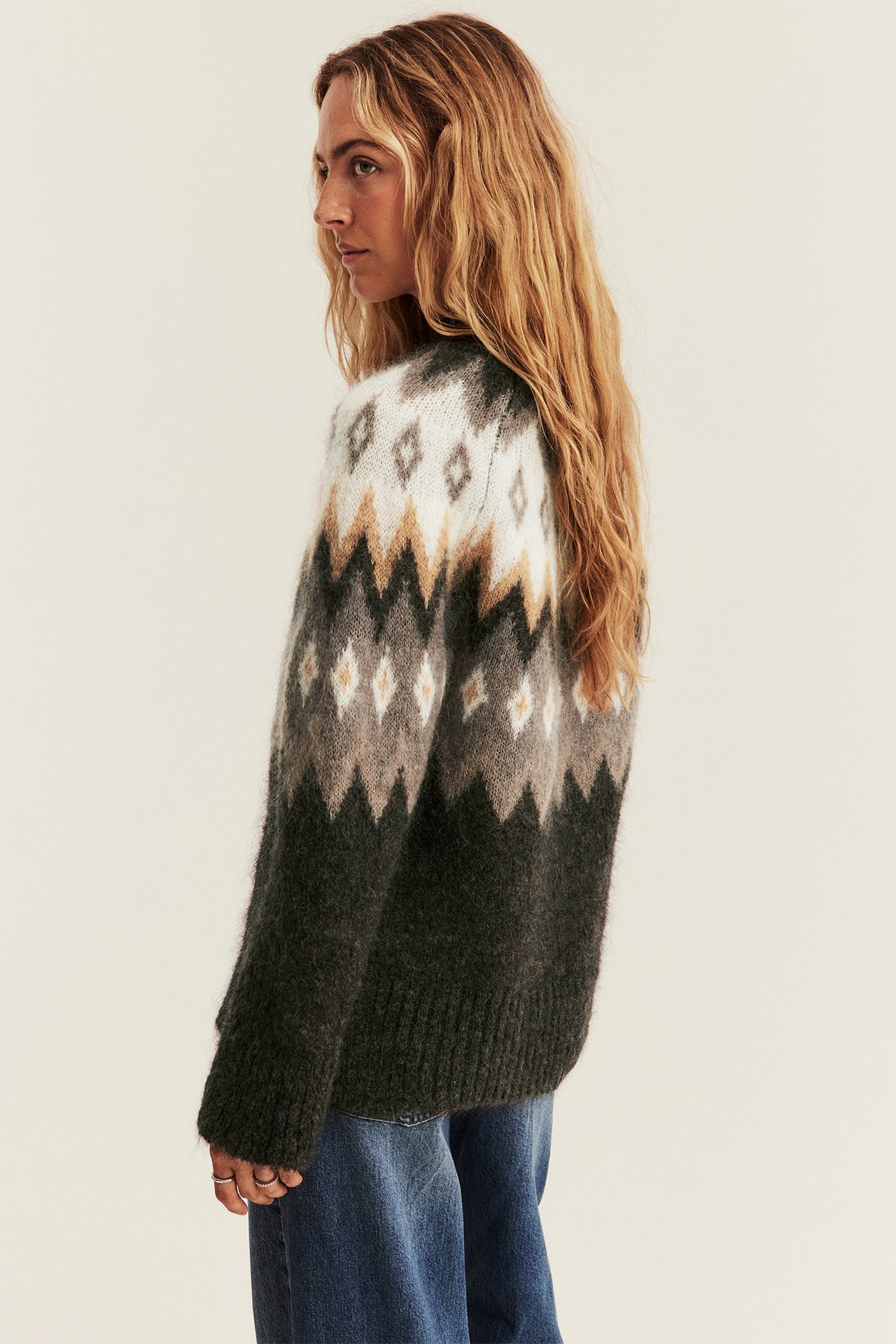 Sidebilde av kvinne i mørkegrønn mønstret fair isle-genser og blå jeans.
