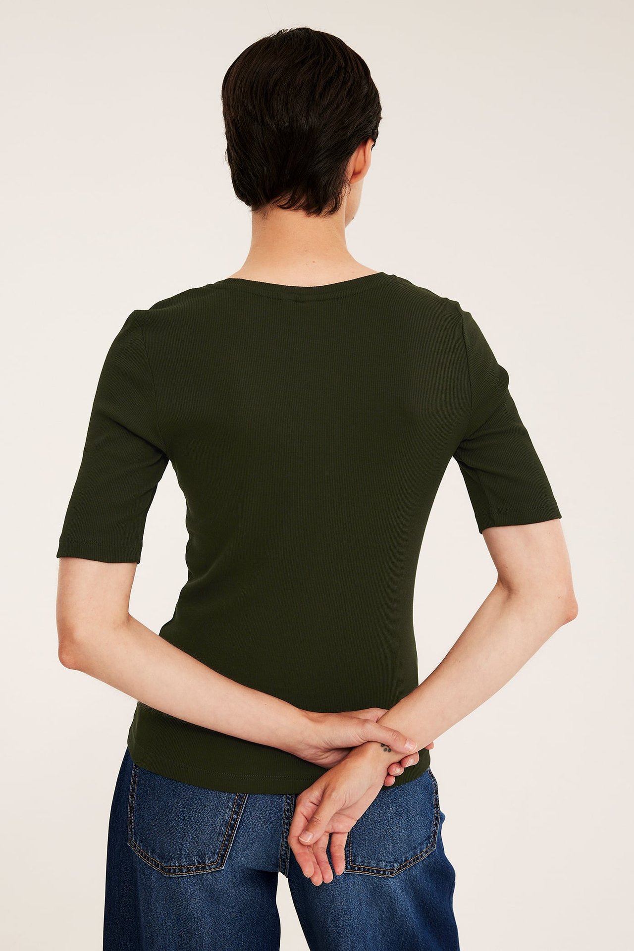 Ryggvy av en kvinna i en åtsittande mörkgrön ribbad kortärmad topp och blå jeans.