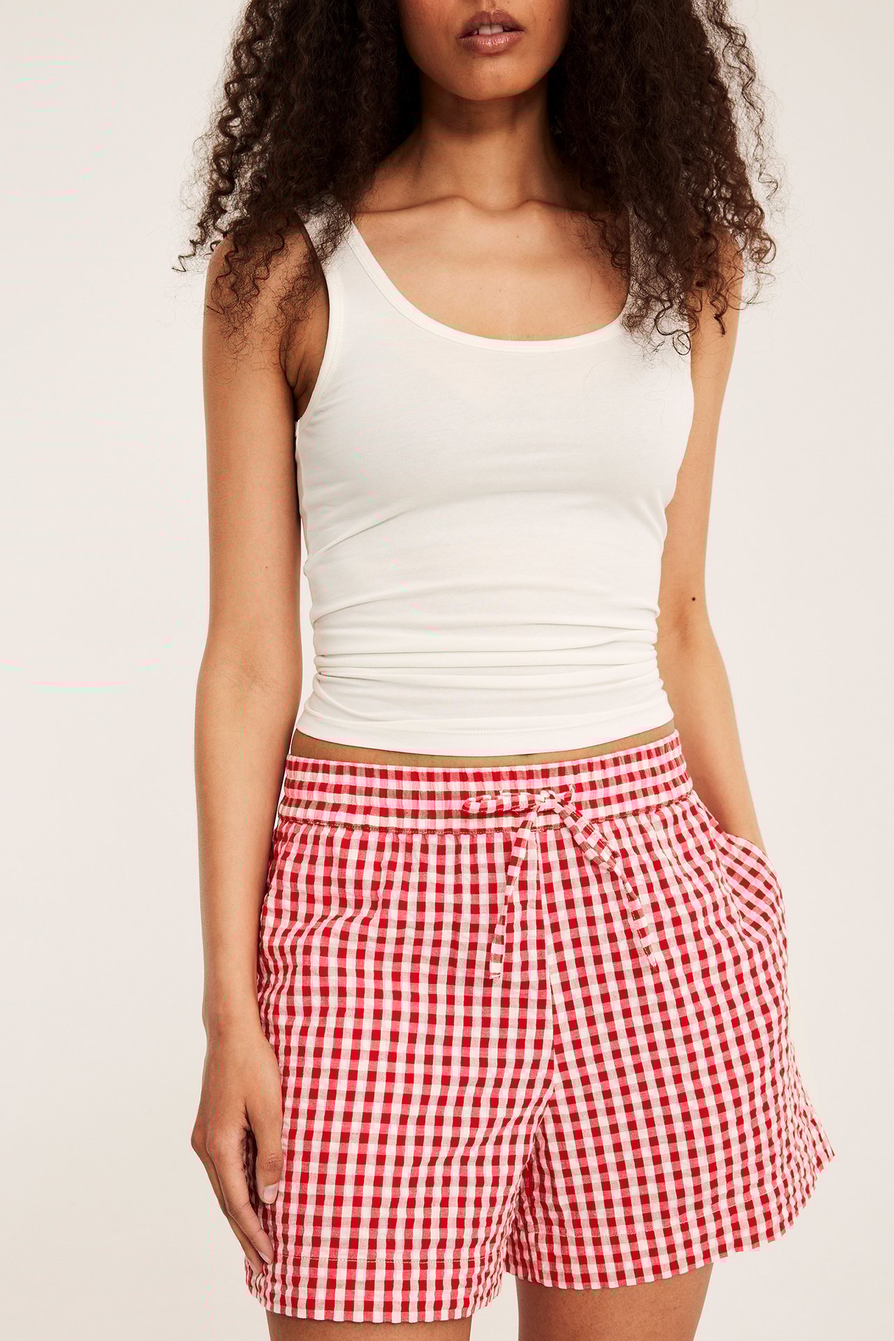 Forfra: kvinne i rødrutete seersucker-shorts med snøring og en hvit singlet.