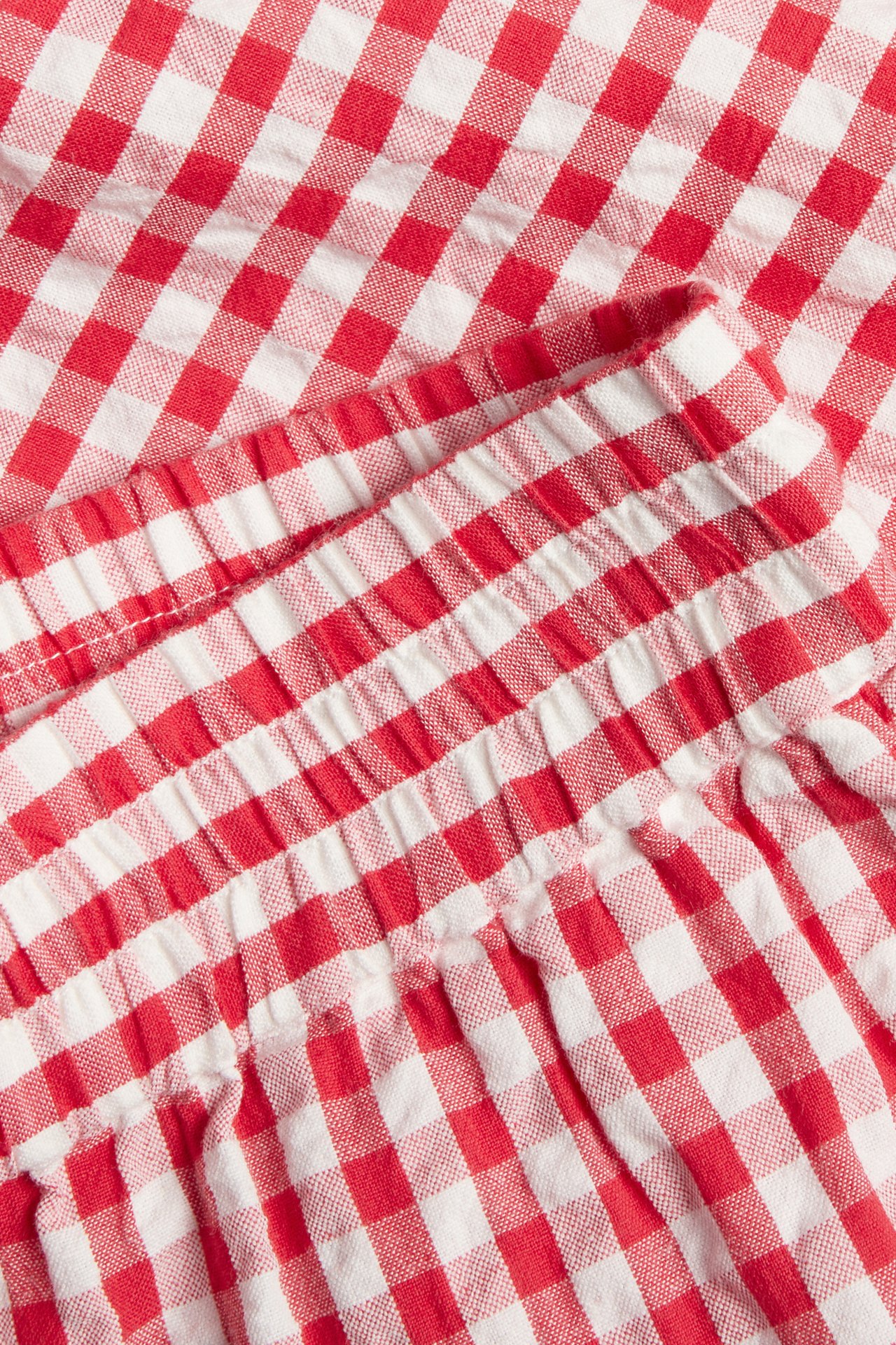 Zbliżenie czerwono-białych szortów seersucker w kratę z elastyczną talią.