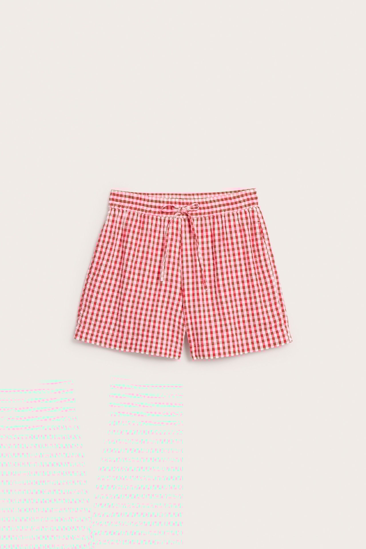 Widok z przodu czerwono-białych szortów z bawełny seersucker w kratę, z białym sznurkiem i kieszeniami.
