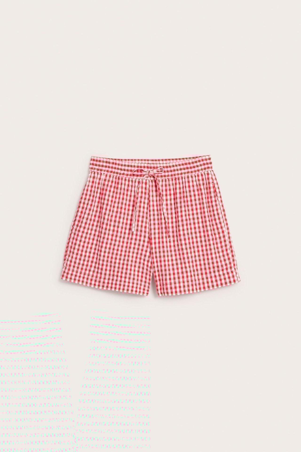 Framsida av röda och vita rutiga bomullsseersuckershorts med vit dragsko och sidfickor.
