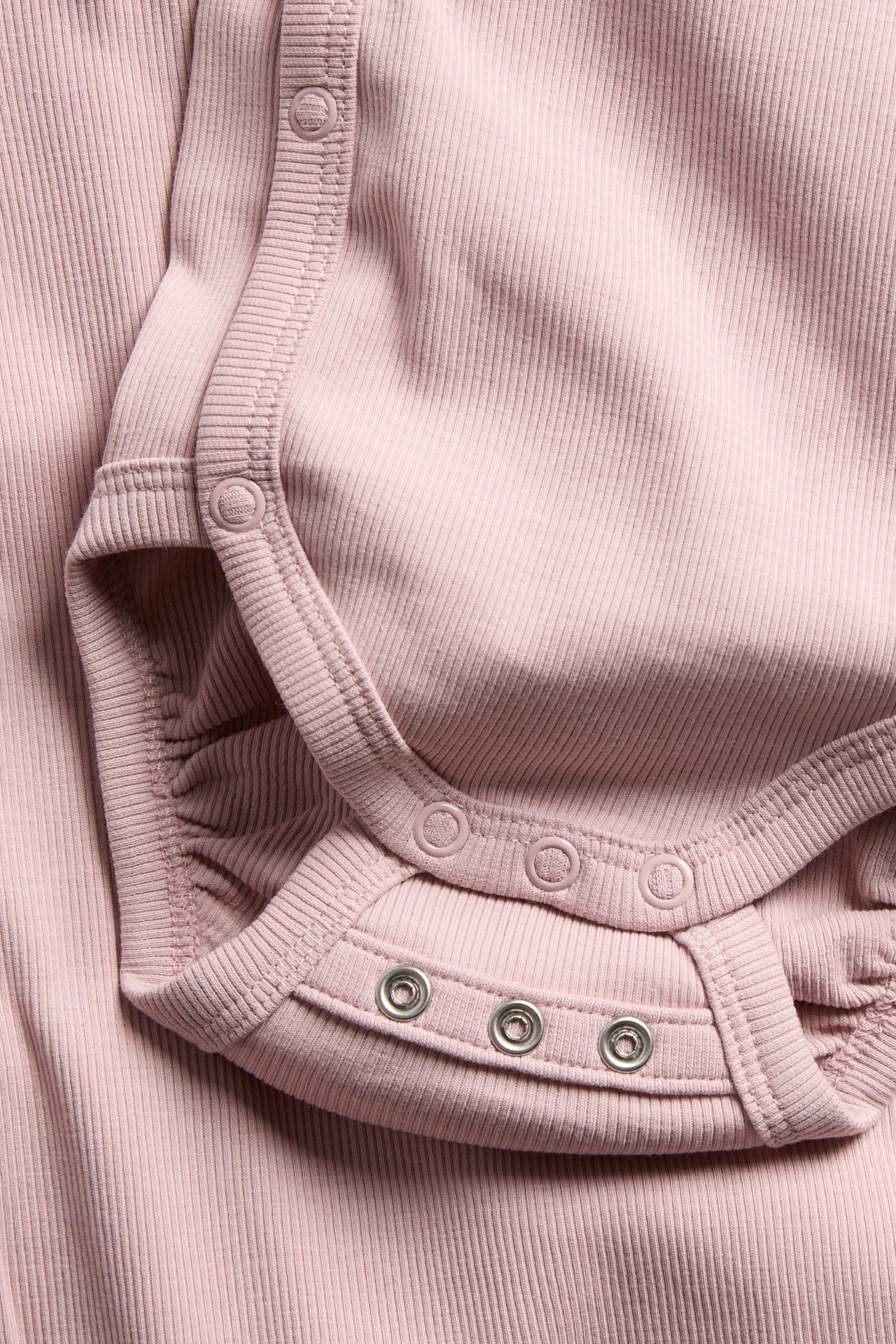 Närbild på en rosa ribbad babybody med tryckknappar i grenen och sidan.