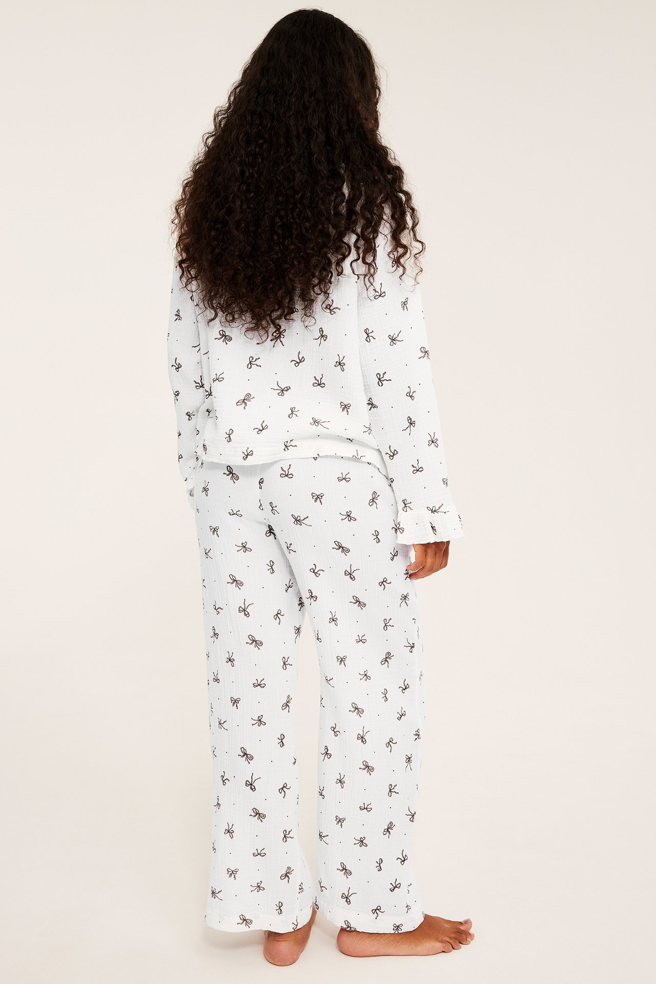 Naisen selkäpuoli valkoisessa pyjamassa, jossa on mustia rusetteja ja pilkkuja.