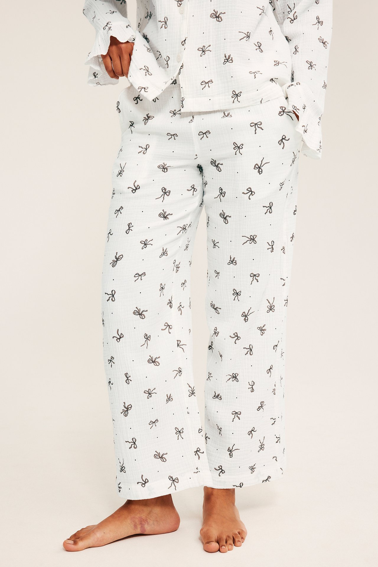 Edestä päin, aikuinen nainen yllään valkoiset pyjamat mustalla rusetti- ja pistekuvioinnilla.