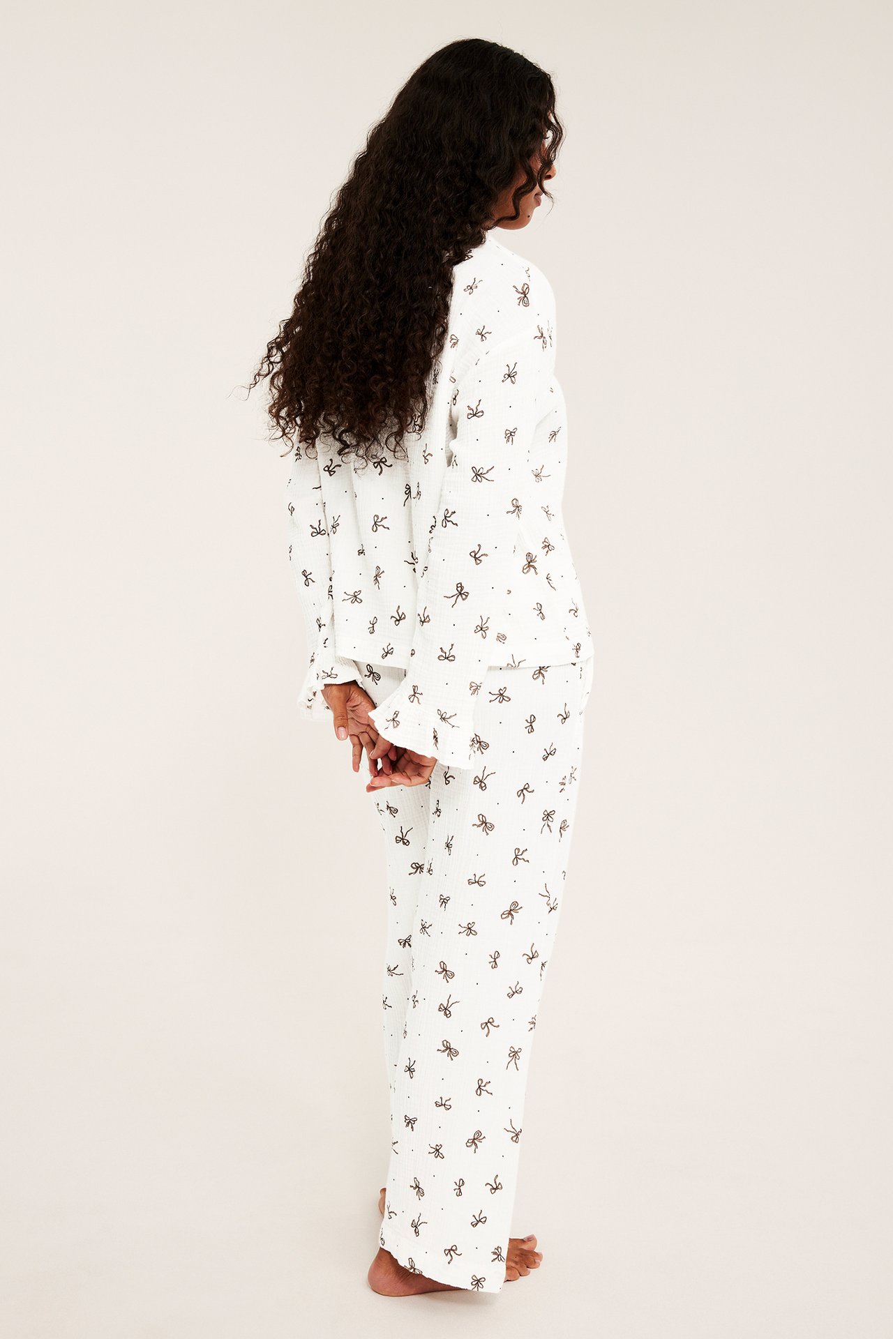Sidebilde av kvinne i hvit, løstsittende pyjamas med sløyfemønster.