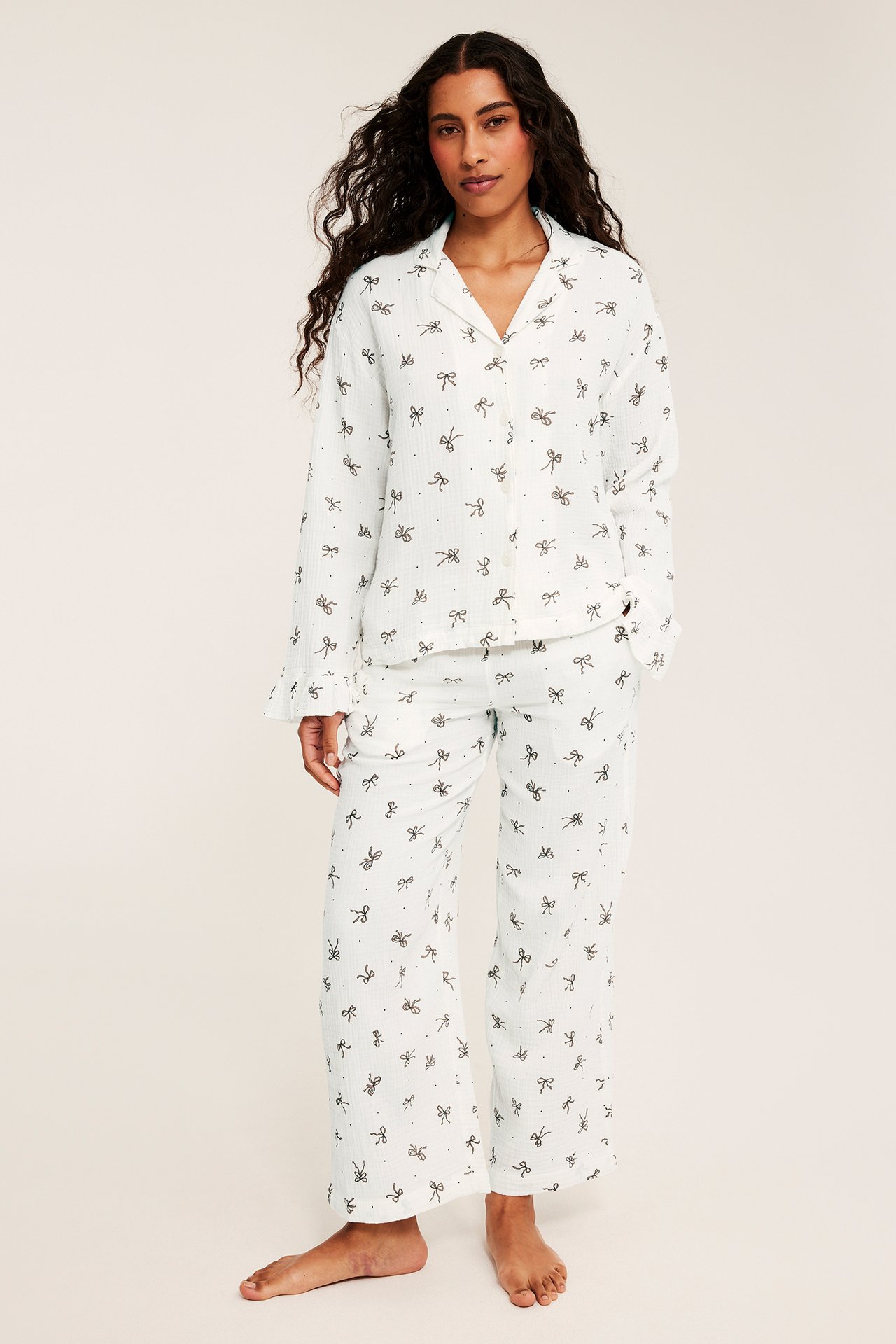 Frontvy på en kvinnlig modell i vit pyjamas med rosett- och prickmönster.