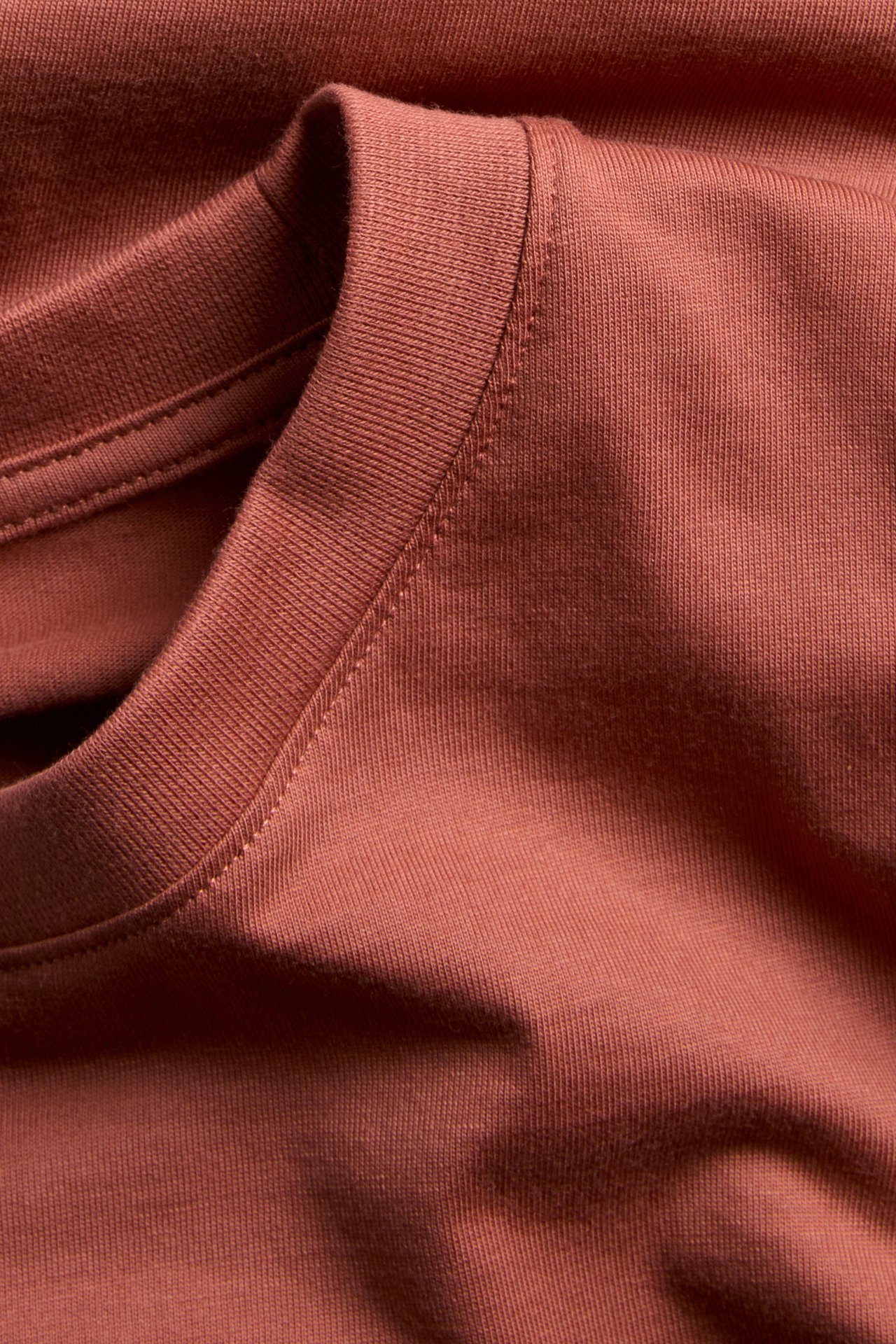Närbild på en roströd t-shirt med ribbad rundhals.