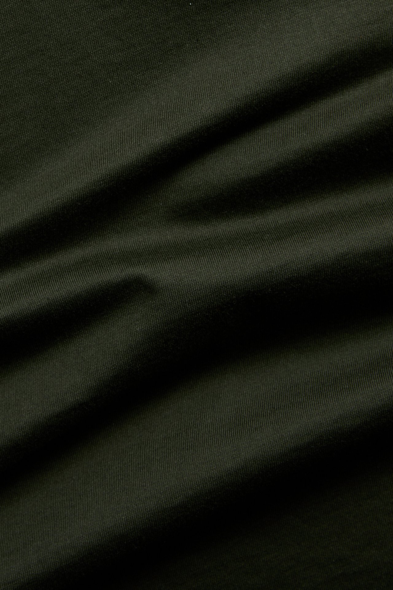 Närbild på mörkgrönt, enfärgat bomullstyg för T-shirt.