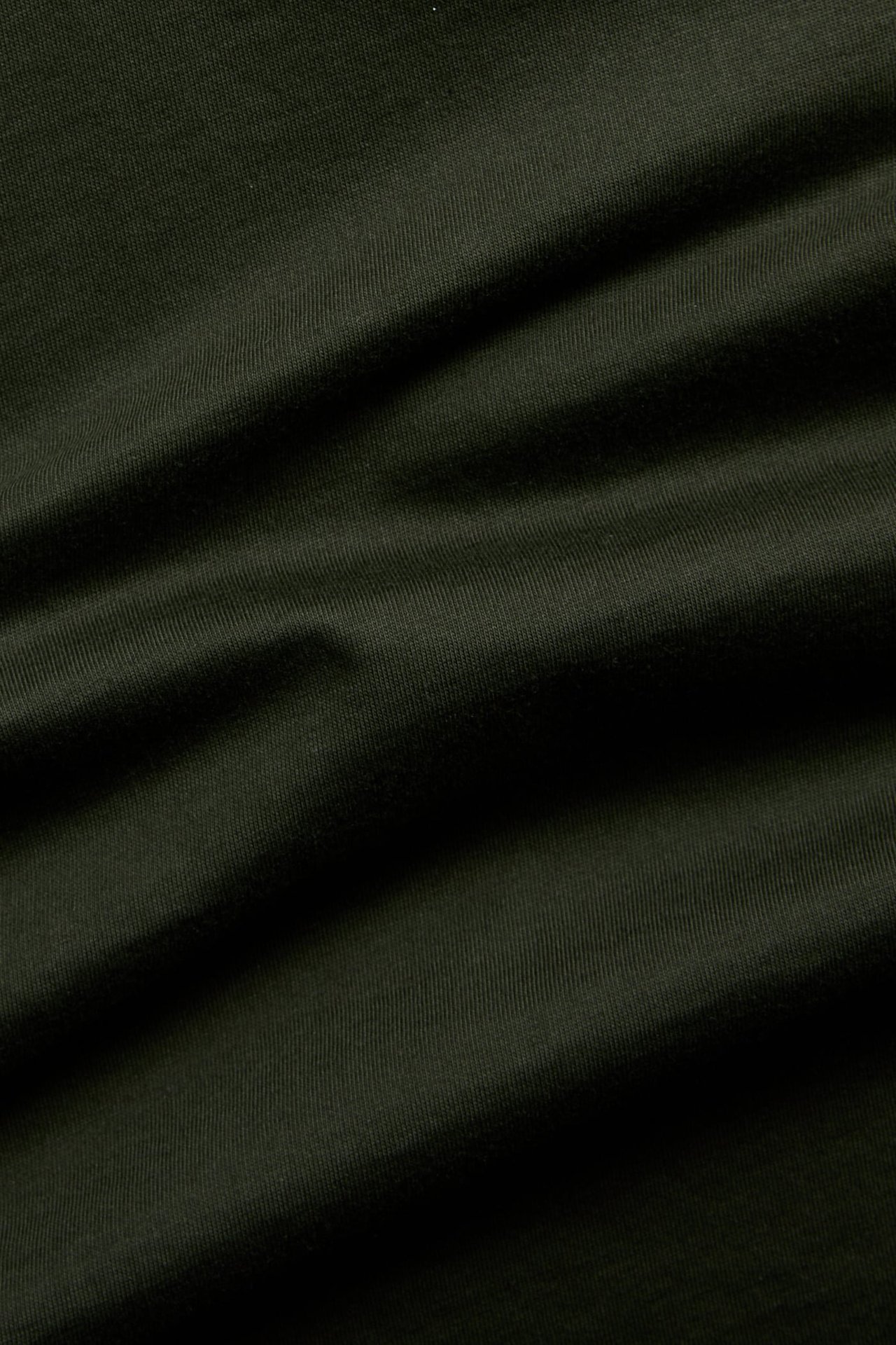 Närbild på mörkgrönt, enfärgat bomullstyg för T-shirt.