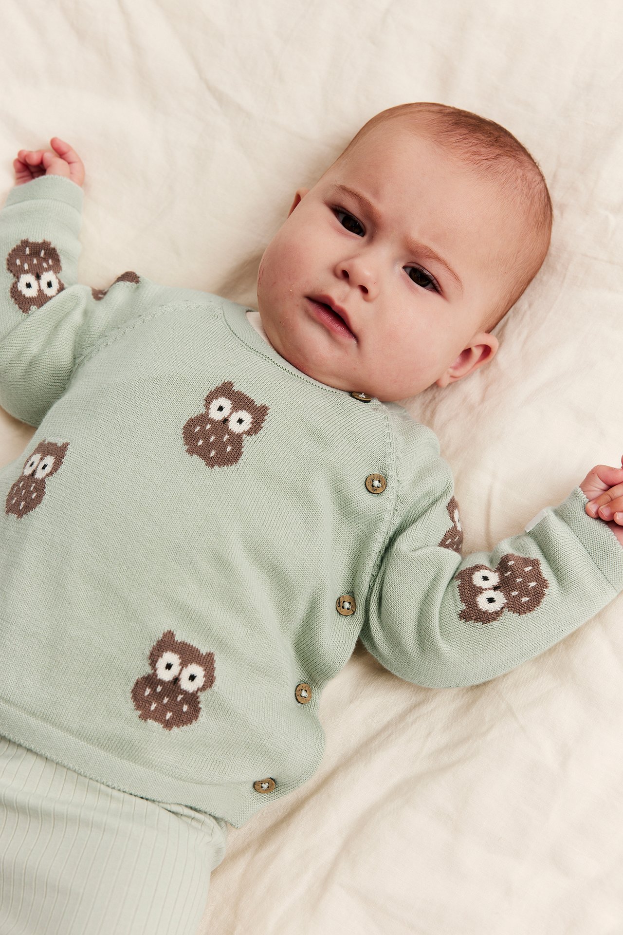 Ovenfra-utsikt av en baby iført mintgrønn strikket ugle-mønstret cardigan med ribbestrikket bukse.