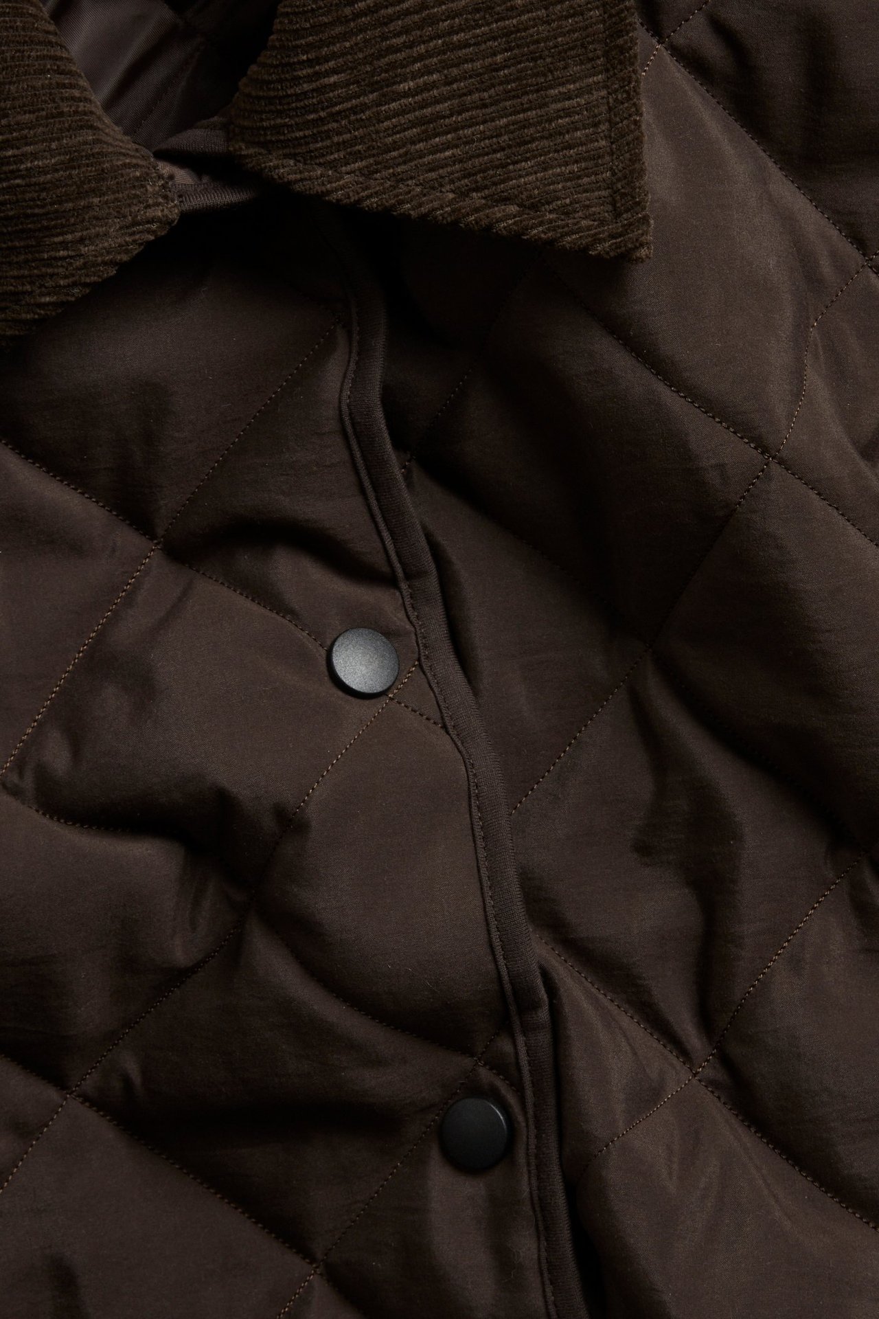 Zbliżenie na ciemnobrązową pikowaną kurtkę ze sztruksowym kołnierzem i czarnymi napami z przodu.